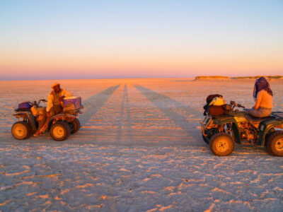 Tourist and guide in glow of setting sun on quad bikes stop while crossing Makgadikgadi Pans National Park, scenic large flat area of salt pan desert to take in view, Botswana